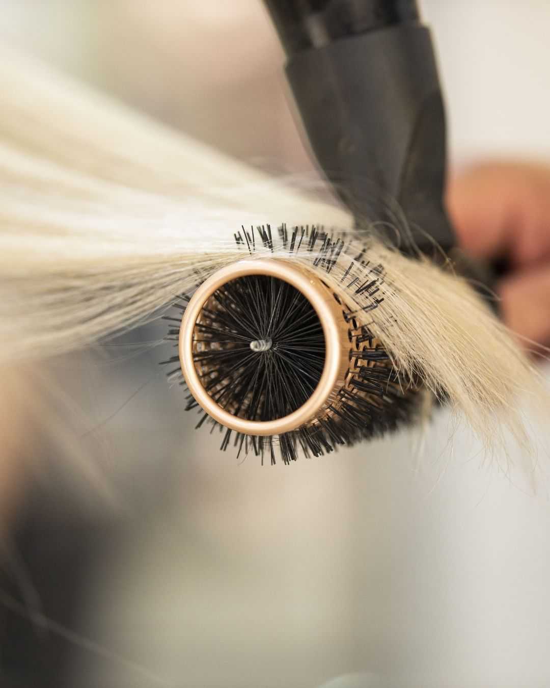 Blow-drying blonde hair with a round brush close-up.