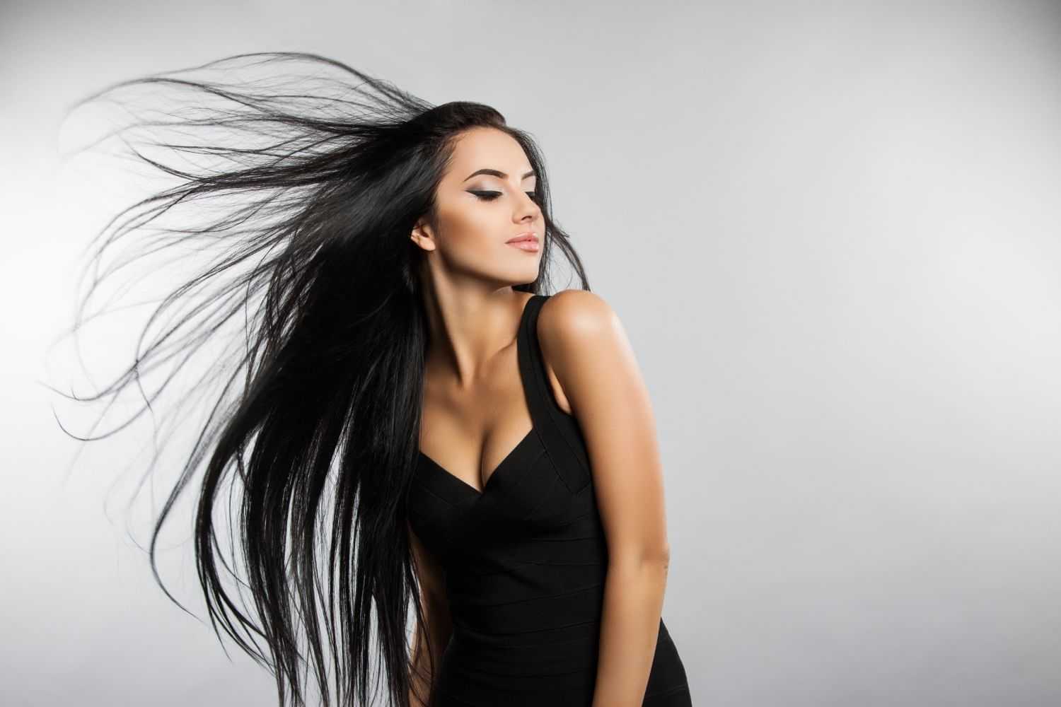 Woman with long, flowing black hair in a black dress, posing against a white background.